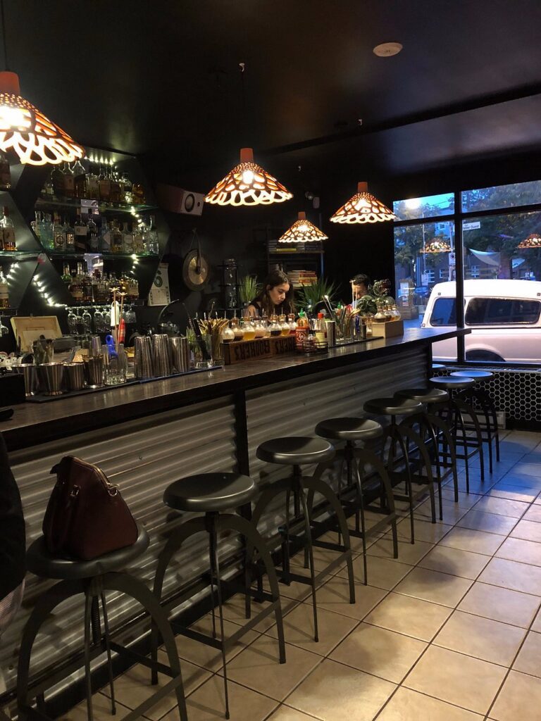 Bar area at Chez Tao!, decorated with warm lighting, stylish stools, and a lively vibe.
