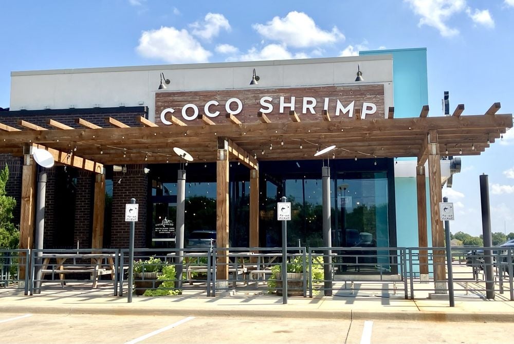 Coco Shrimp restaurant exterior with a wooden pergola and patio seating.