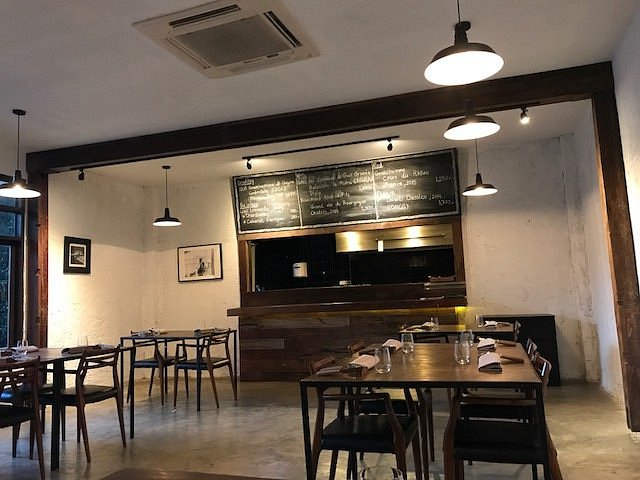 Cuisine De Garden interior with simple wooden furniture, chalkboard menu, and warm lighting.