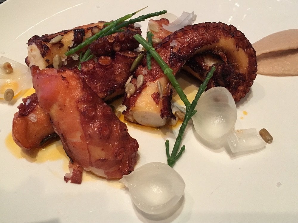A gourmet plate of grilled octopus at Ferreira Café, garnished with pearl onions, seeds, and sea greens.