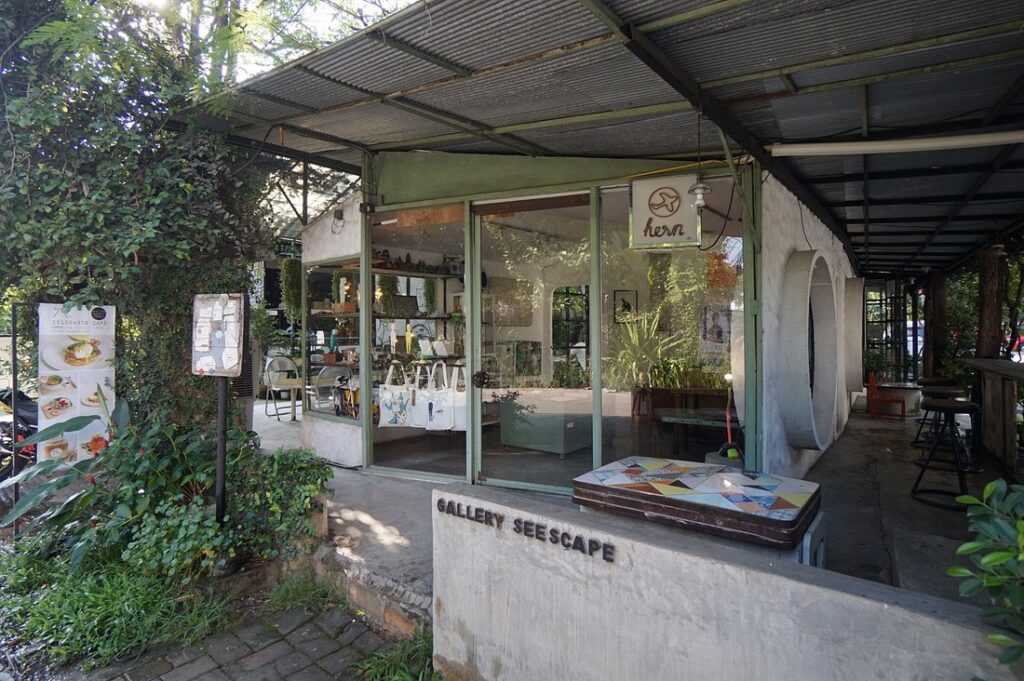 Entrance of Gallery Seescape in Chiang Mai, a cozy art café with glass walls and greenery.