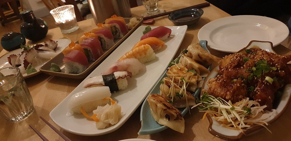 A table at Harajuku Kitchen filled with assorted sushi, gyoza, and crispy sesame chicken.