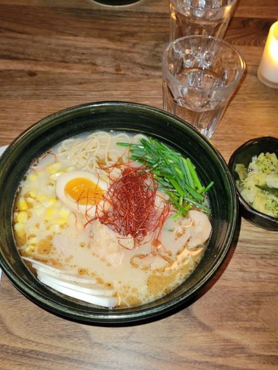 A hearty bowl of ramen at Honō Ramen, topped with egg, pork, and vibrant garnishes.