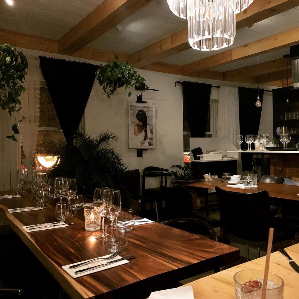 The intimate interior of India Rosa with wood beams, plants, and soft candlelight on polished tables.