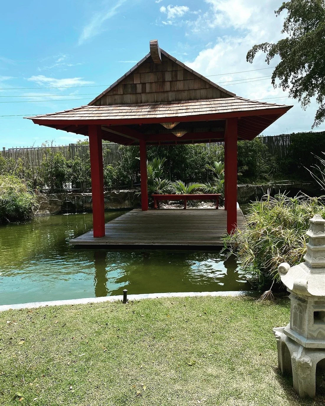 Traditional wooden pavilion over koi pond in Japanese Garden Ponce with stone lanterns and tropical plants