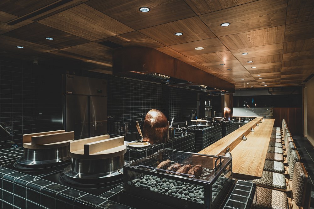 Elegant counter seating and open kitchen at Kyoto Tempura Ten no Meshi with warm wood and black tile decor.