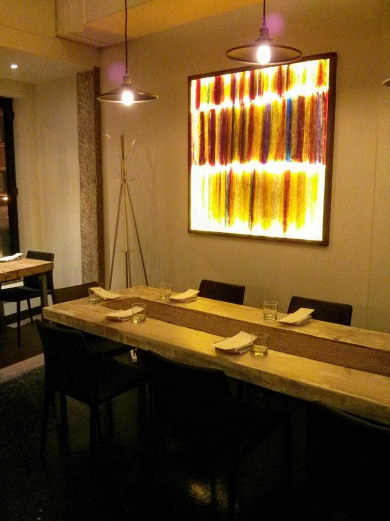 A cozy table at Le Mousso with dim lighting, a wooden live-edge table, and a glowing abstract wall art piece.