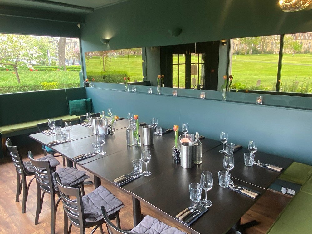 A neatly set dining table inside Left Field, with large windows overlooking a green park.