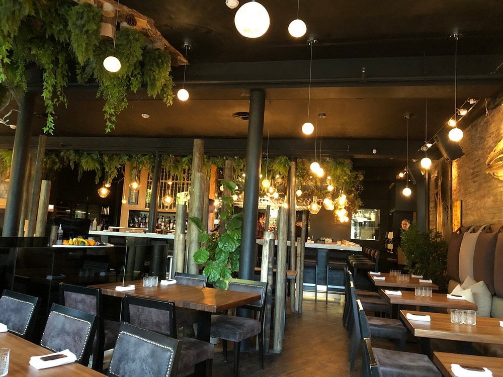 Elegant interior of Légende, featuring moody lighting, wooden decor, and lush greenery above the bar.