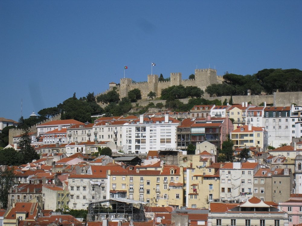 Colorful hillside buildings in Lisbon with São Jorge Castle on the hilltop under a clear blue sky.