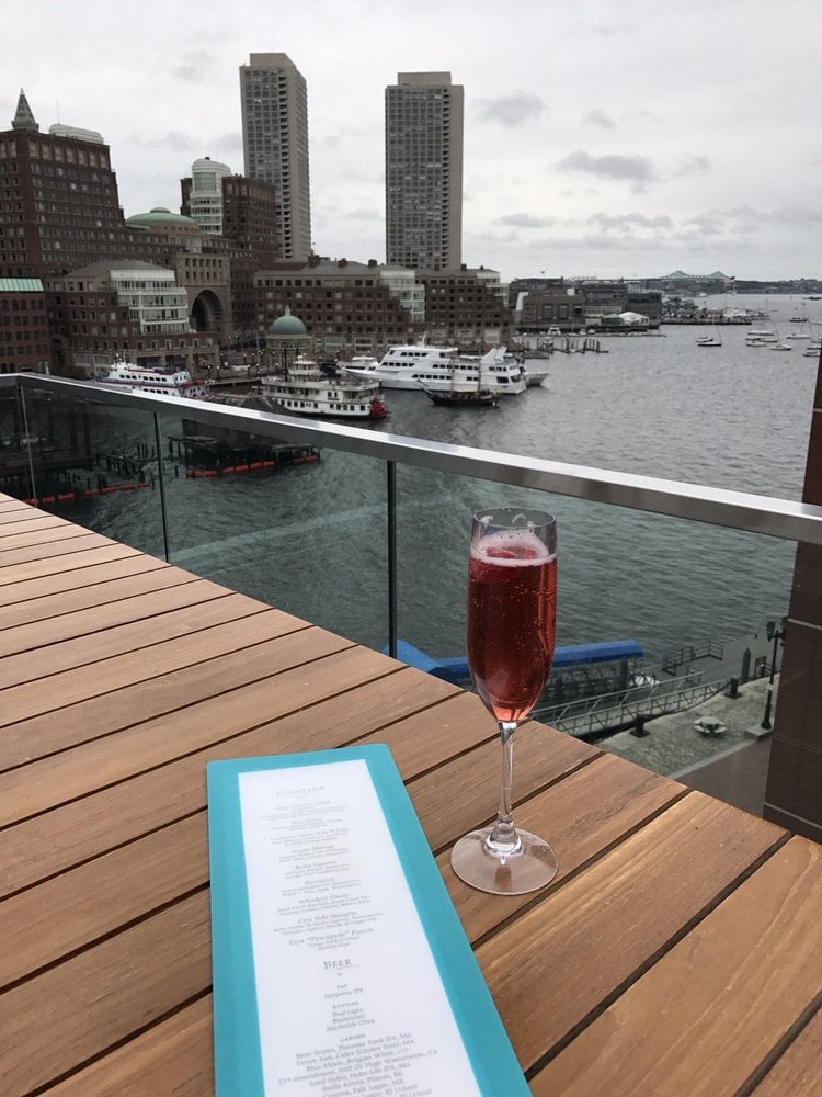 Glass of red cocktail on rooftop table overlooking Boston Harbor.
