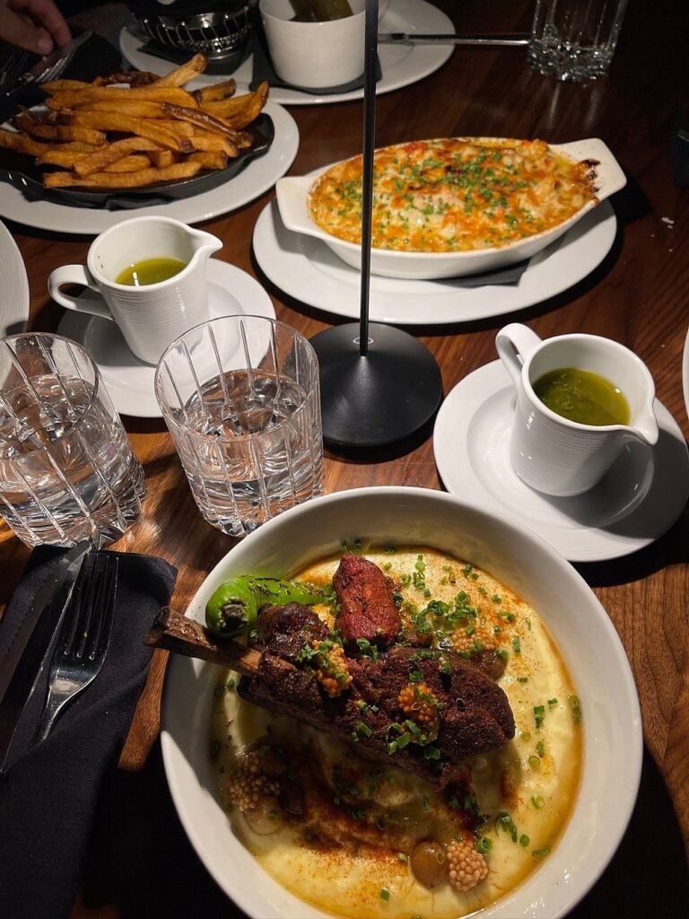 A hearty meal at Moishes with lamb over creamy polenta, served alongside fries and baked seafood casserole.