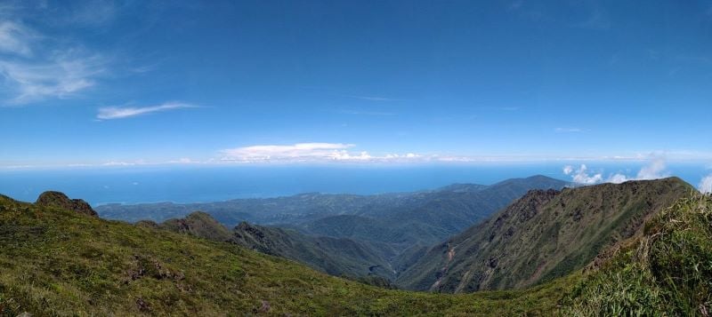 A panoramic view from the summit of Mount Guiting-Guiting, showcasing lush greenery and towering peaks against a clear blue sky