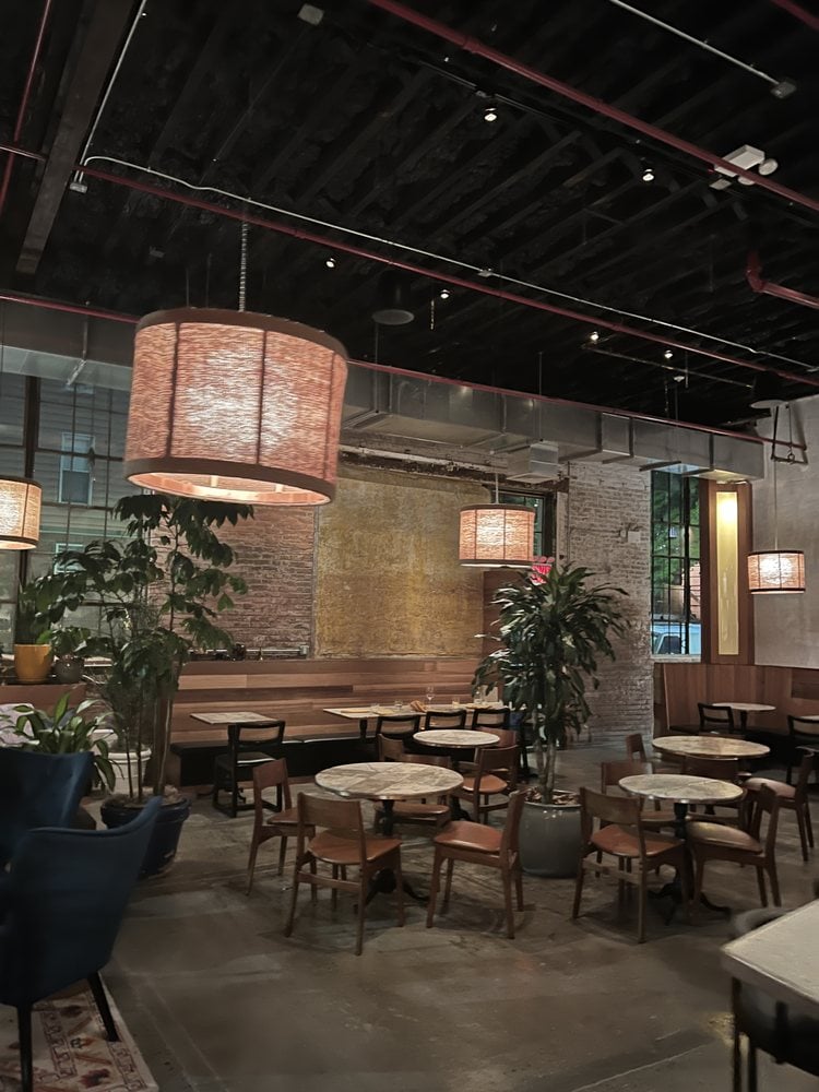 Spacious interior of Nura with modern decor and round marble tables.