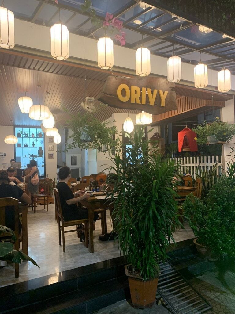Indoor-outdoor dining area of Orivy with wooden furniture, potted plants, and glowing lanterns.