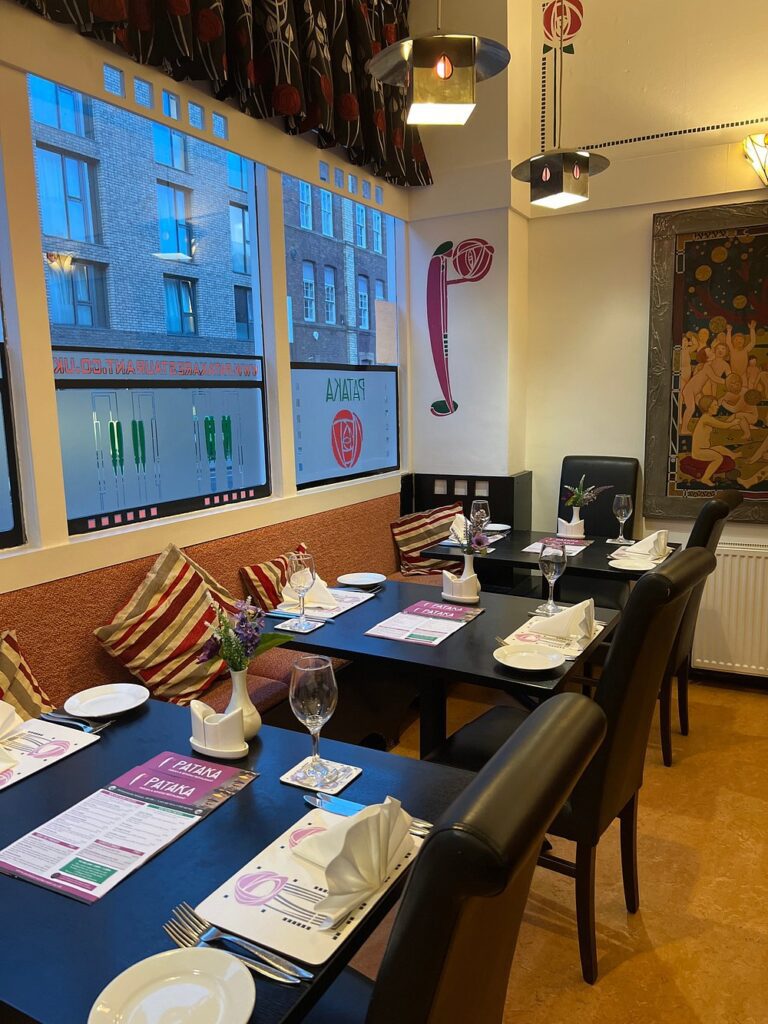 A cozy and colorful dining area at Pataka, set with menus, wine glasses, and striped pillows.