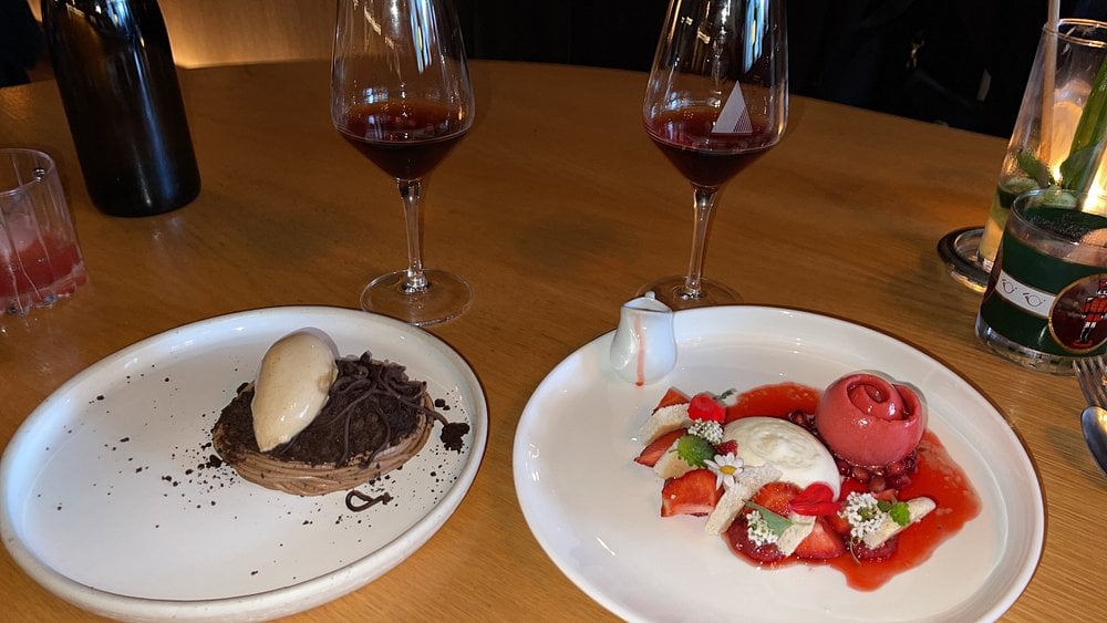 Elegant desserts at Ratafia with wine glasses, featuring chocolate and berry-themed plates on a wooden table.