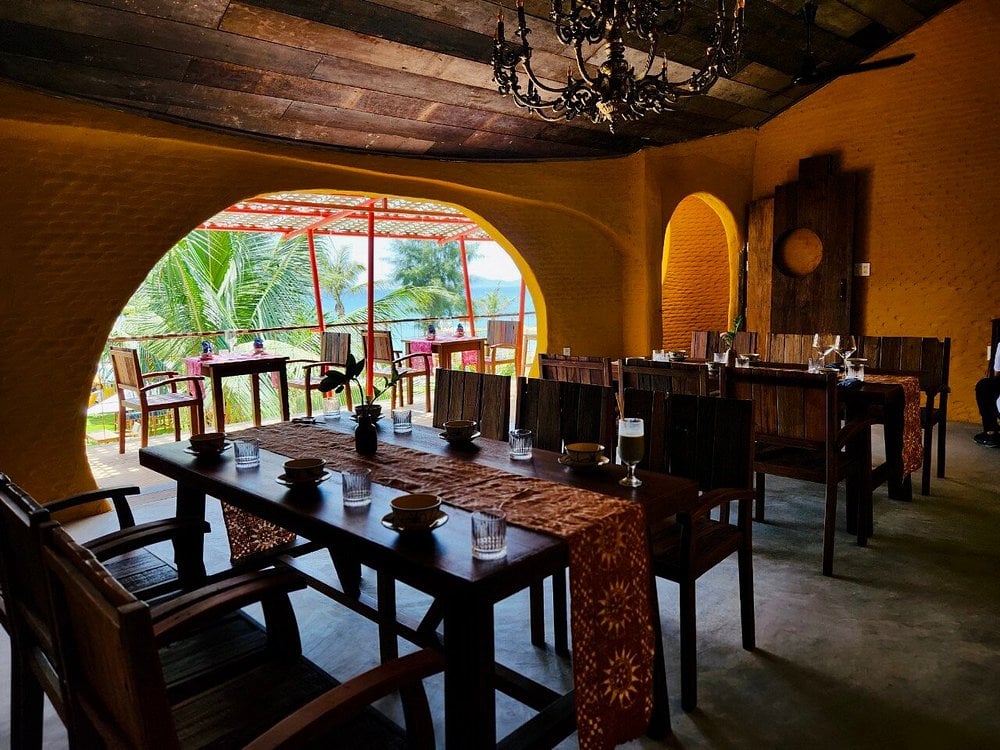 Cozy and rustic dining space at Salt Hoian with wooden furniture and an open view of palm trees and the sea.