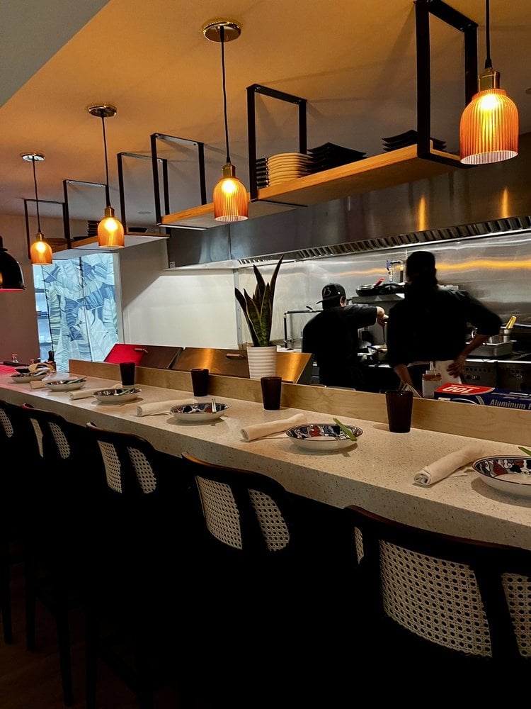 A sleek chef’s counter at Satu Lagi with hanging lights, open kitchen, and place settings ready for service.