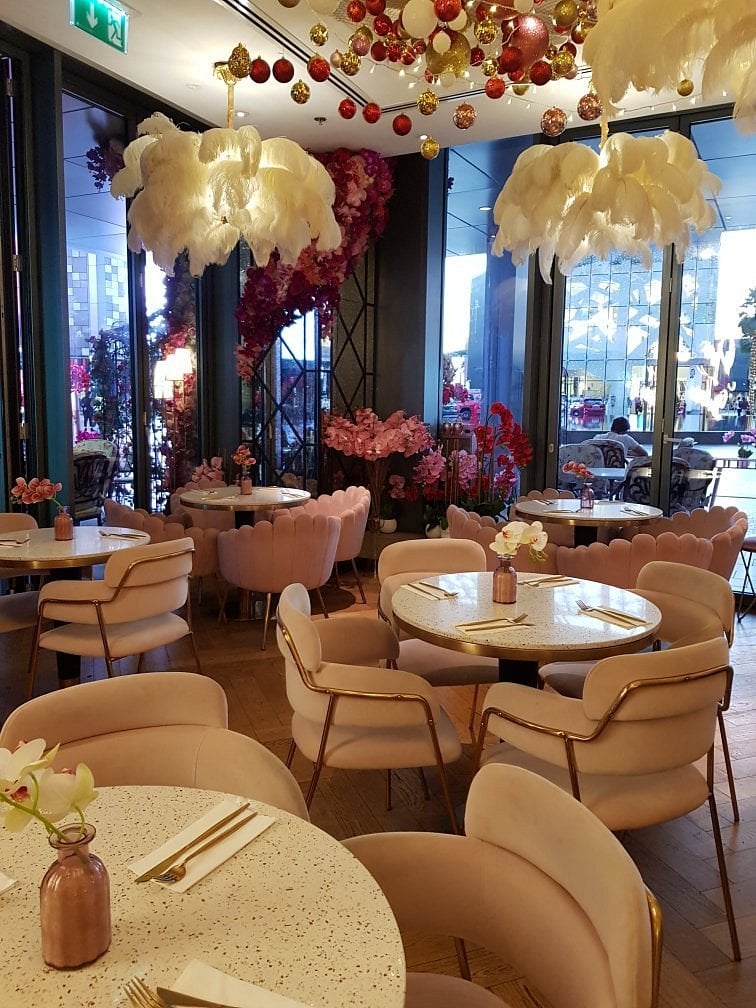 Saya Café interior decorated with pink chairs, floral arrangements, and feather chandeliers.