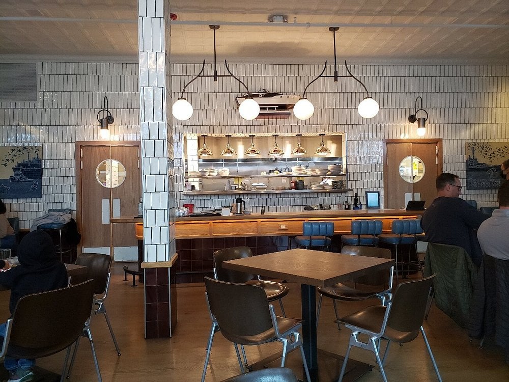 Interior of Seabird featuring tiled walls, globe lights, and an open kitchen behind the bar.