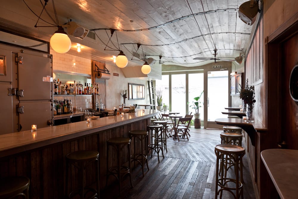 Rustic bar and dining area inside St. Mazie with warm ambient lighting.