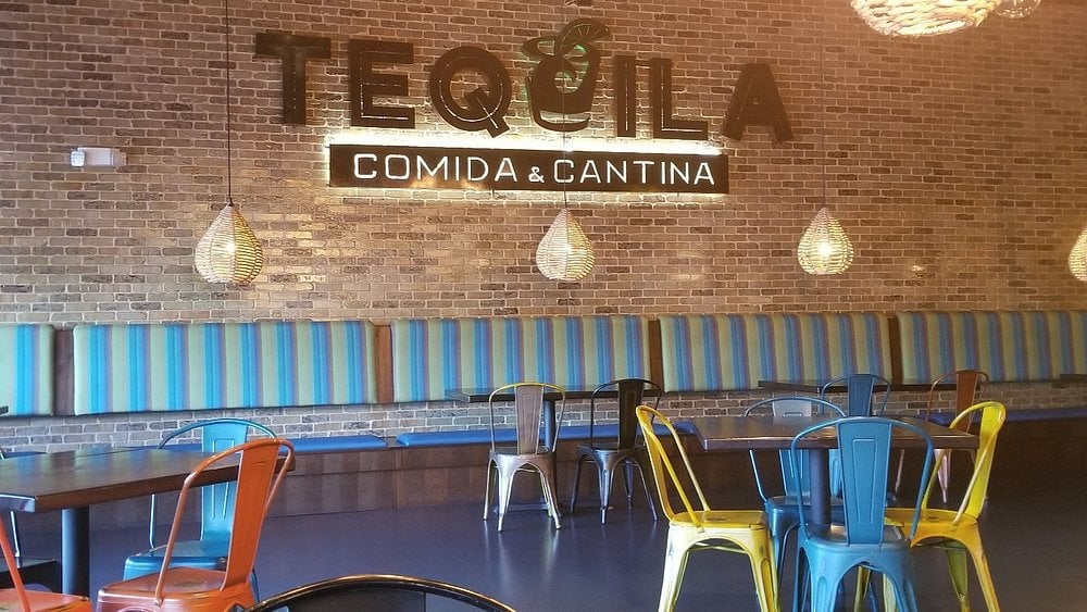 Interior of Tequila Comida & Cantina with colorful chairs and a striped booth along a brick wall.
