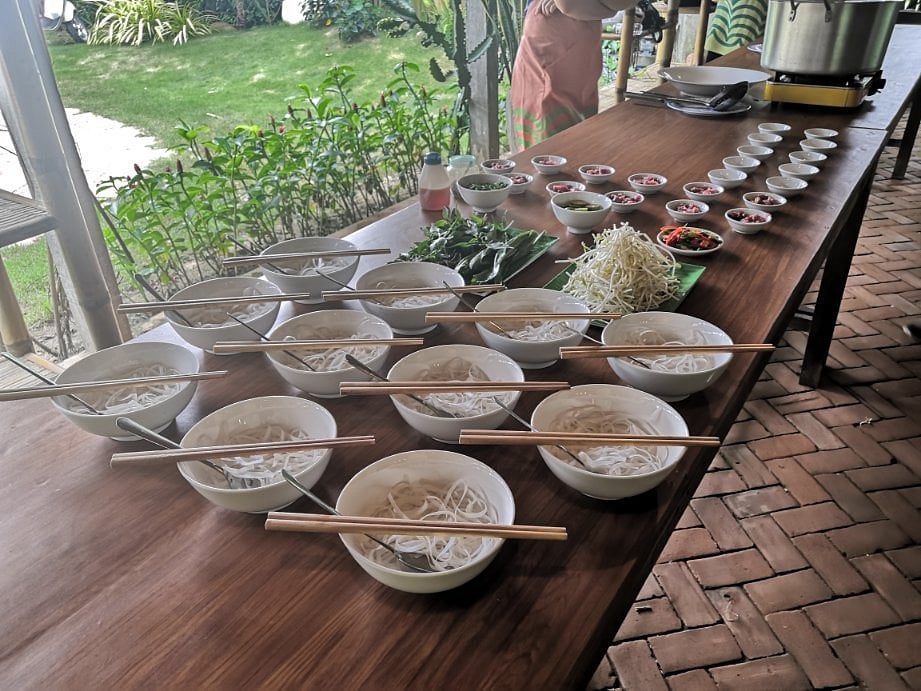 A table at Thuan Tinh Island is set up for a Vietnamese cooking class with bowls of noodles and fresh ingredients.