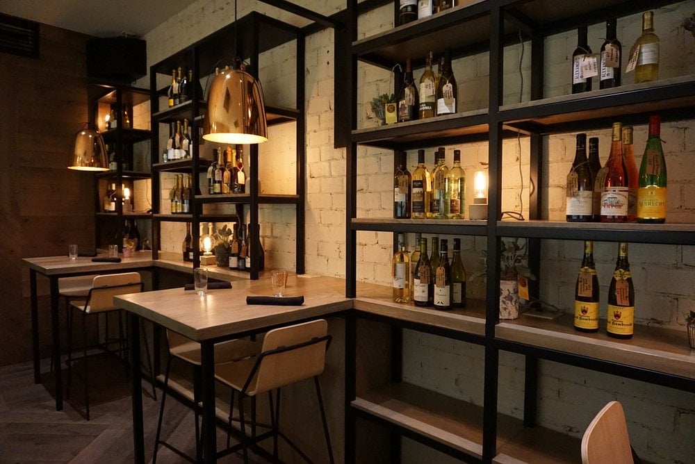 Modern wine bar seating at Town Hall with bottles on display shelves.