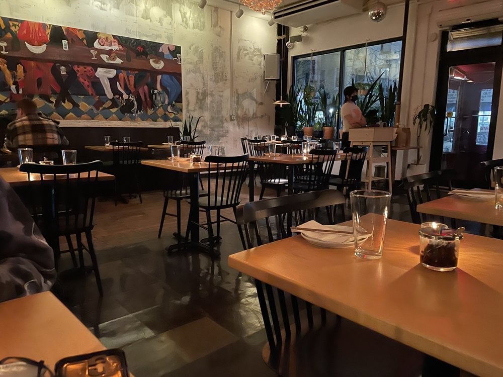 Casual dining setup inside Win Son with a lively mural and wooden tables.