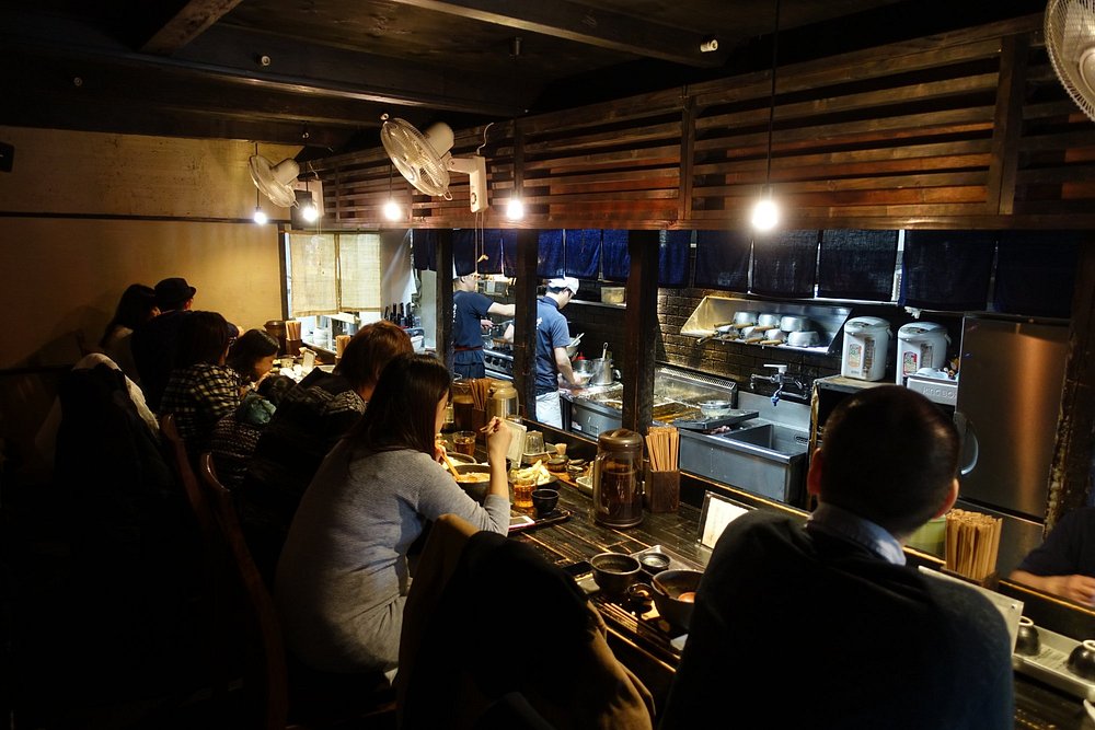Crowded counter seating at Yamamoto Menzou with open kitchen.