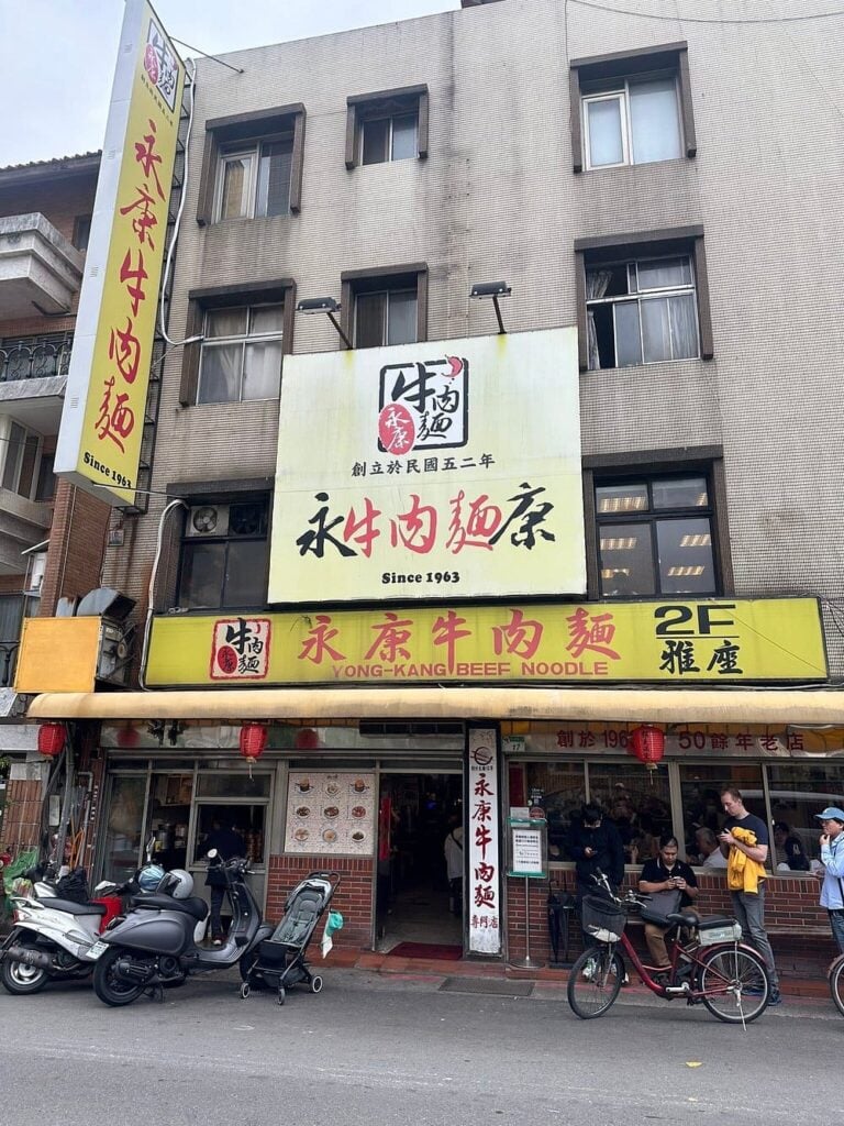 Exterior of Yong-Kang Beef Noodle restaurant with people and scooters in front.