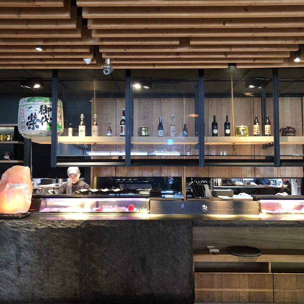Sushi counter at TAN ZUO MA LI with a chef and bottle display.