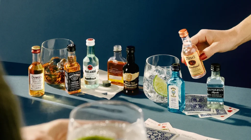A hand reaches for a mini Tito's vodka bottle among a variety of miniature liquors and cocktails on an airplane tray table