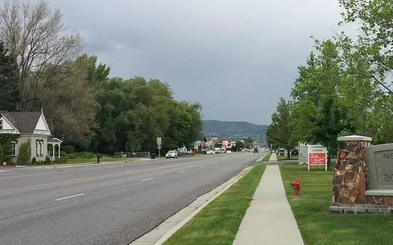 A suburban street scene with homes, trees, and mountains faintly visible in the background.