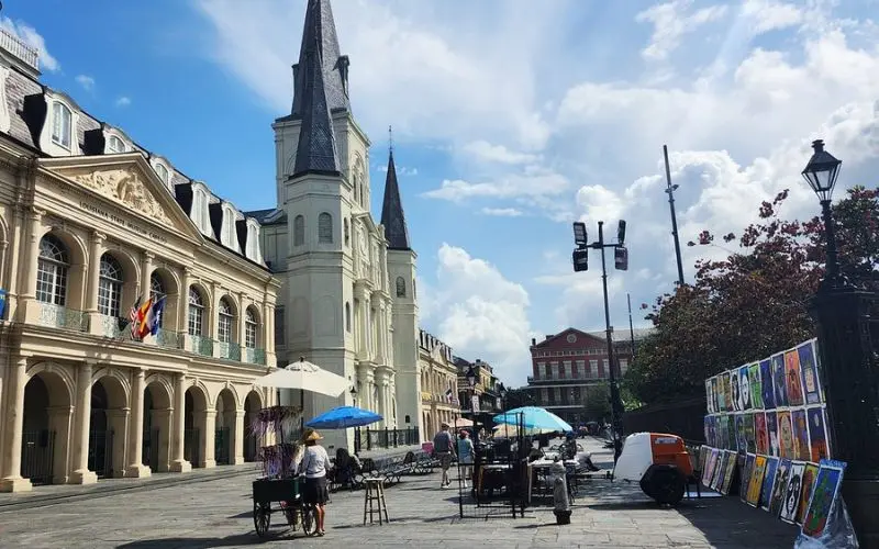 Jackson Square with artists and umbrellas in front of a white cathedral under a bright sky.