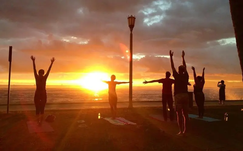 Group practicing yoga at sunset on a Hawaii beach.