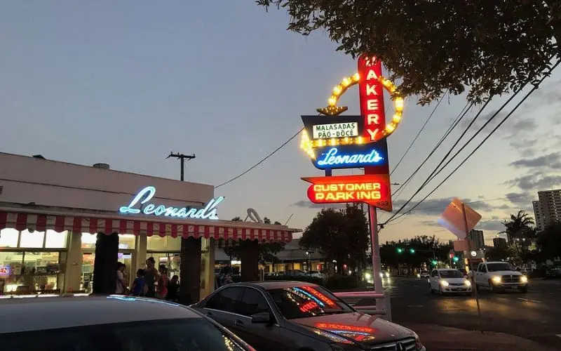 Exterior of Leonard’s Bakery with its glowing sign at dusk.