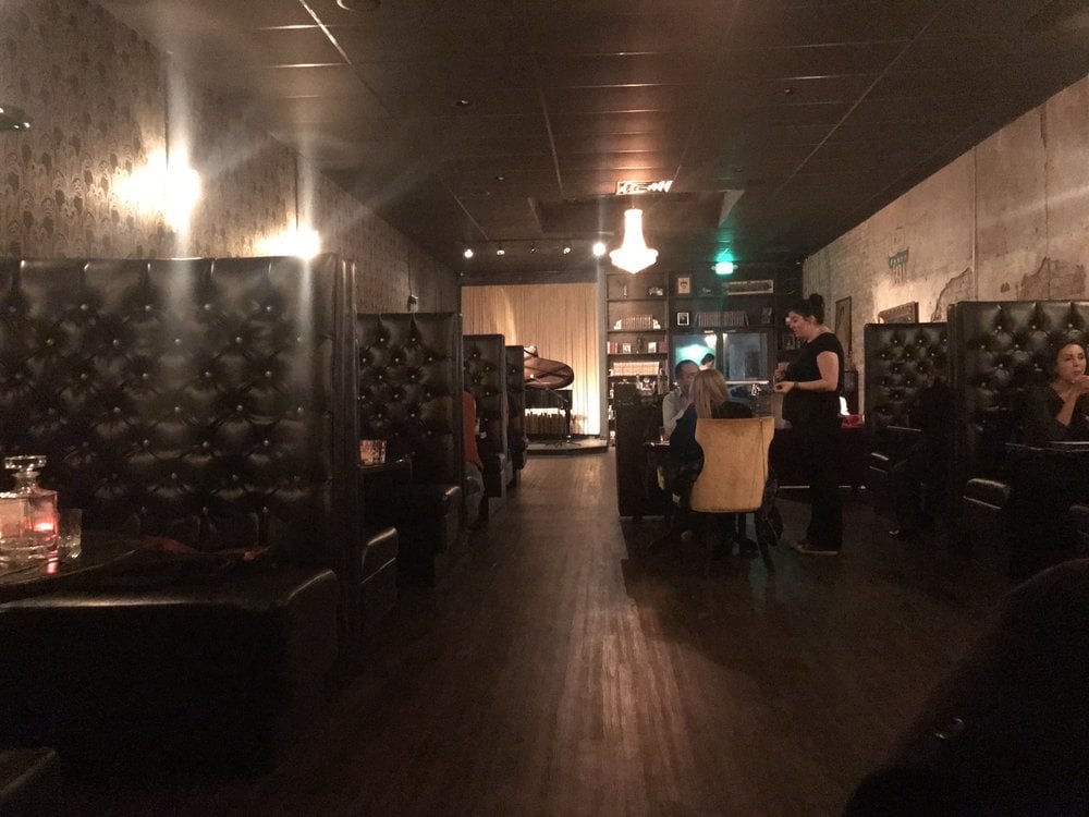 Dimly lit interior of 1922 with leather booths, dark wood floors, and a grand piano in the back.