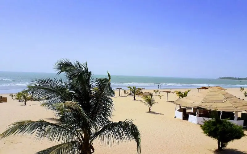 Sanyang Beach in Gambia with palm trees and huts by the ocean.