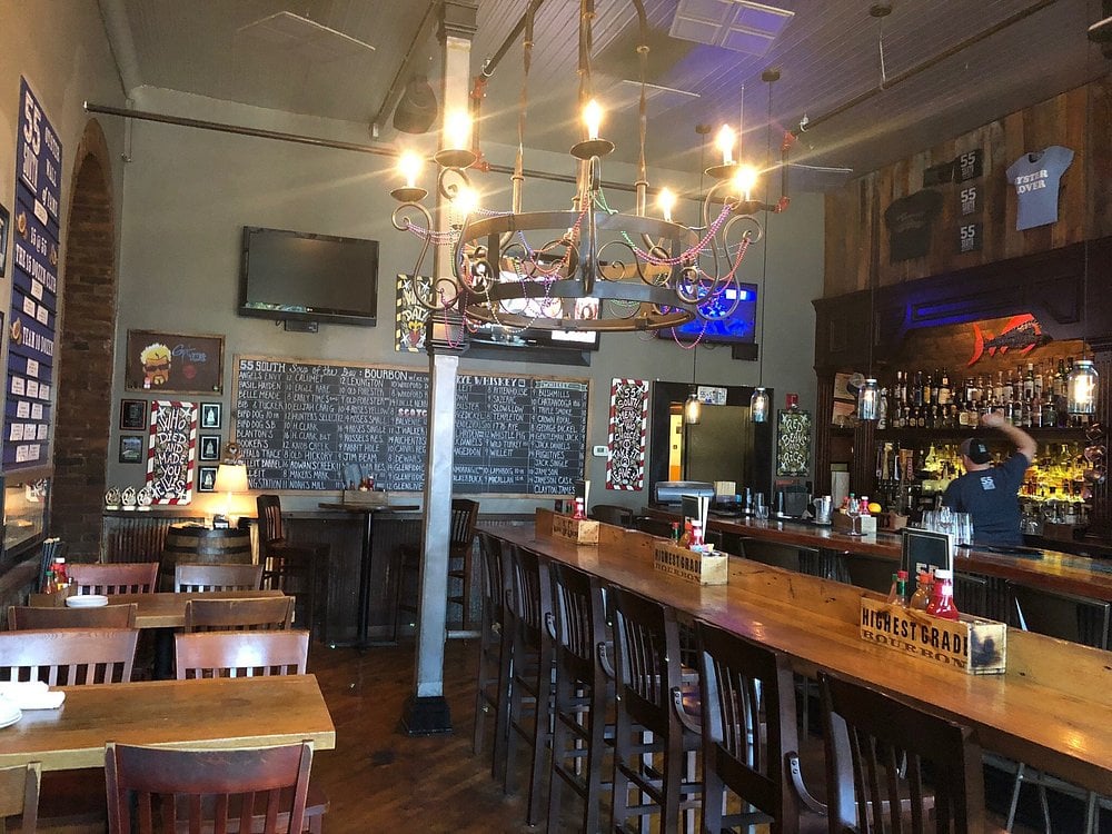 Lively bar area at 55 South with a bourbon-themed menu board and rustic-industrial decor.