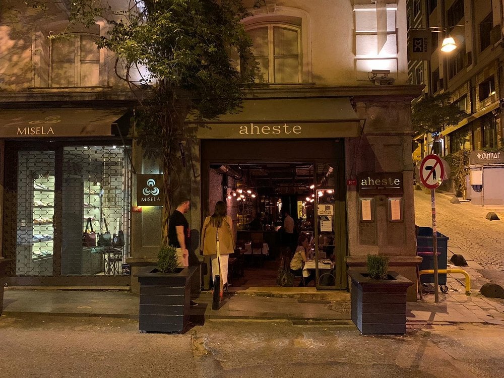 Nighttime exterior view of Aheste restaurant with guests entering.