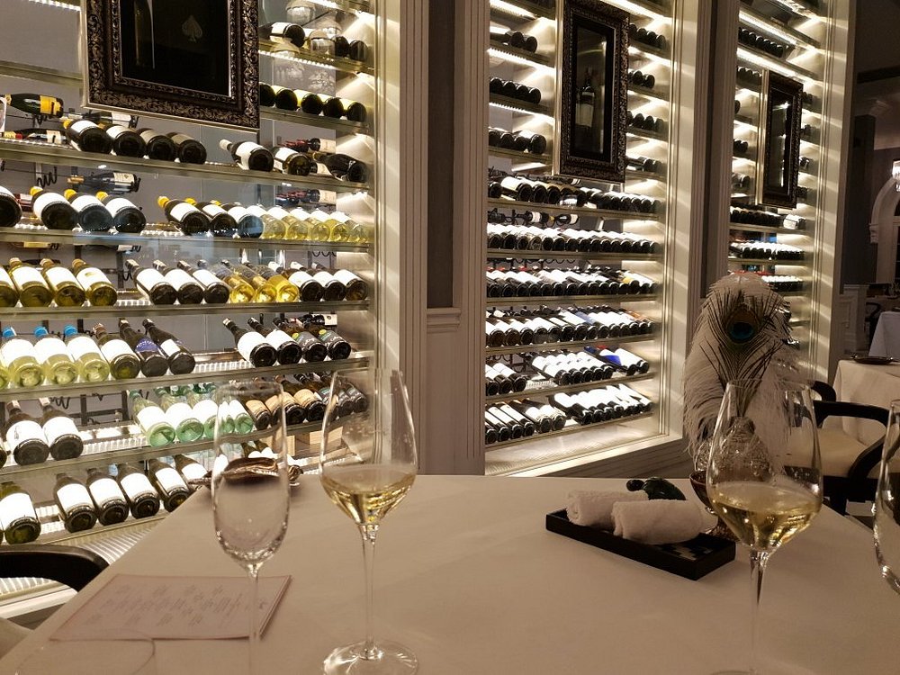 Elegant wine room at Apéritif with backlit shelves full of bottles and a refined table setting.