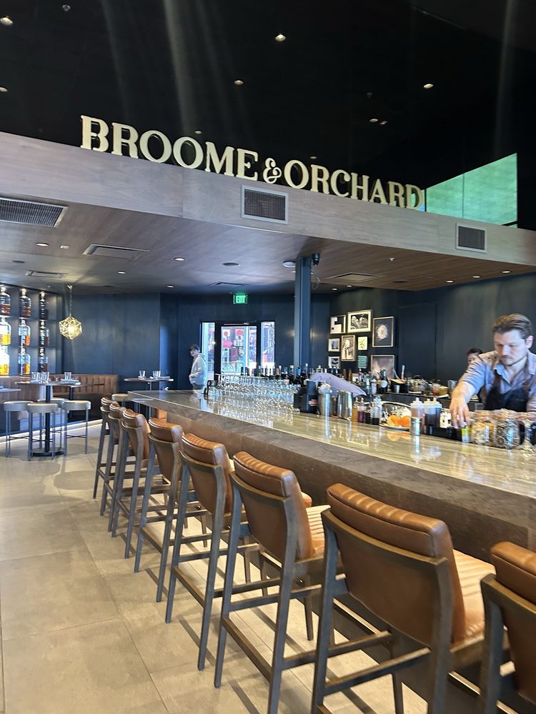 Modern interior of Broome & Orchard with a sleek bar, leather stools, and upscale decor.