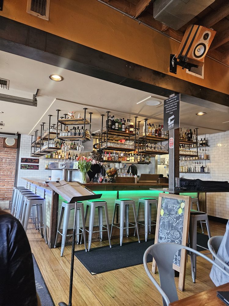 Modern bar setup at Centro Bar & Kitchen with hanging liquor shelves and a glowing green counter.