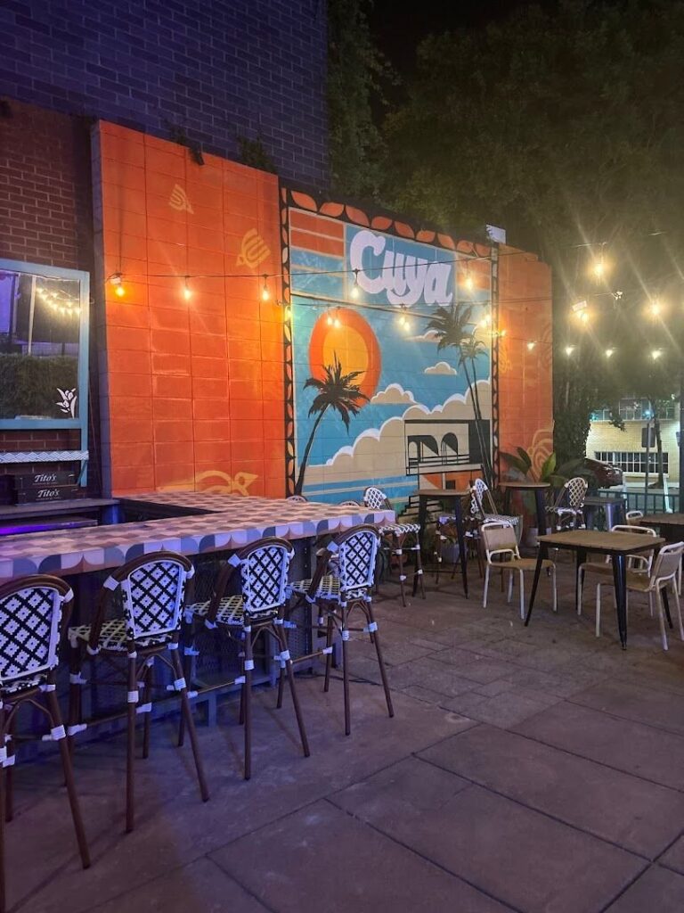 Outdoor patio at Cuya Cocina Latina with string lights, tropical mural, and colorful seating.