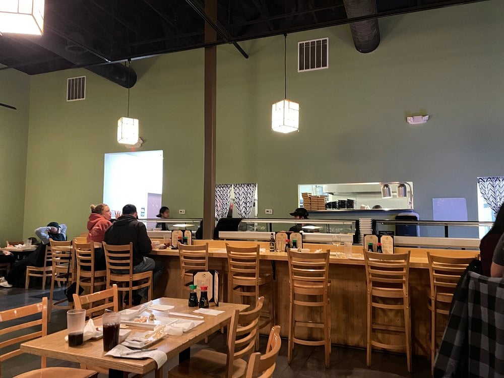 Casual dining room at Hinoki Sushi with a sushi bar, light wood furniture, and minimalist decor.
