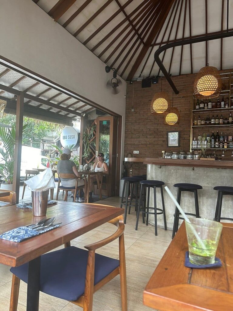 Casual tropical dining area at IBU SUSU Bar & Kitchen with a sleek bar and open-air seating.