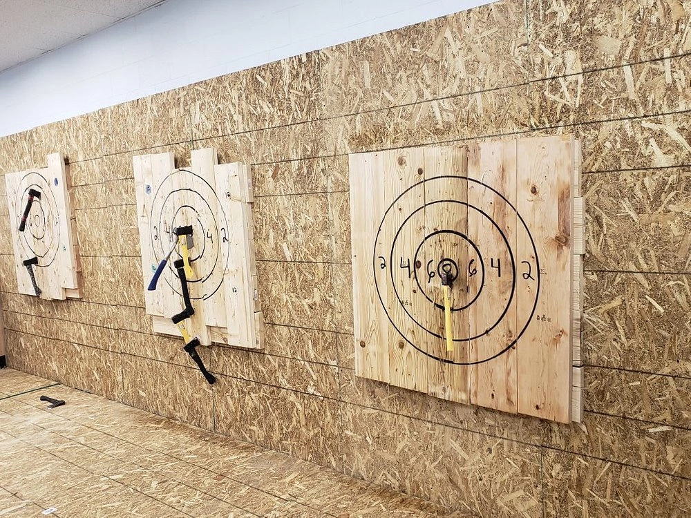 Axe throwing targets mounted on wooden wall at Jack Axe Throwing in Myrtle Beach, showing stuck axes and ninja stars in bullseye targets