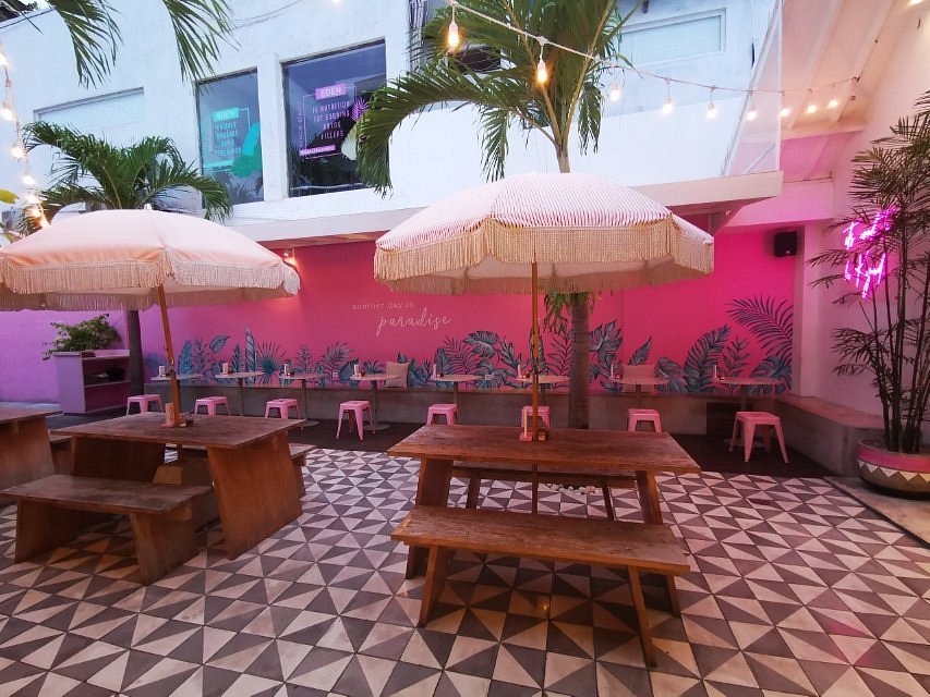Bright and playful pink outdoor seating area at KYND Community with palm trees and string lights.